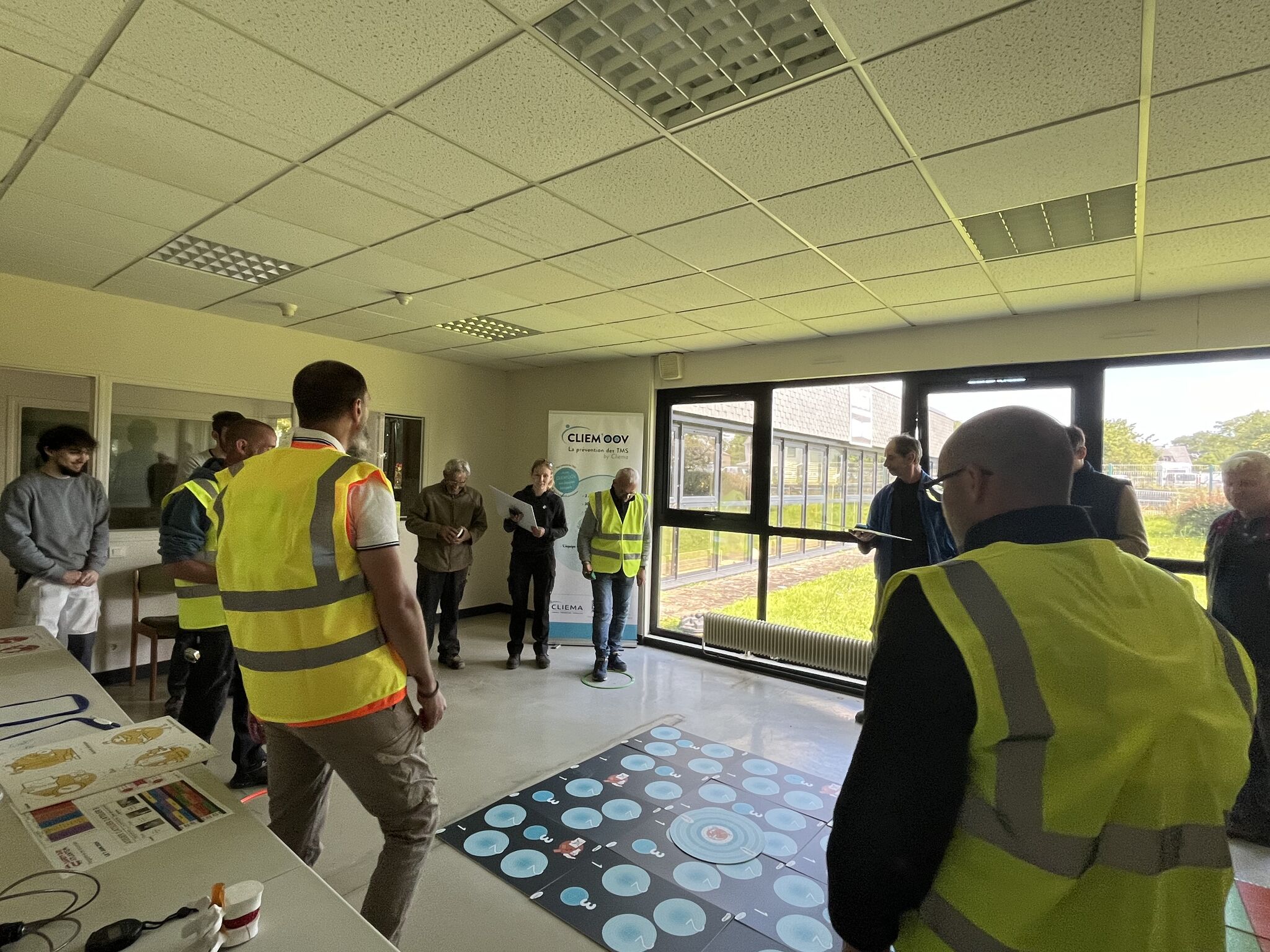 Groupe de personnes portant des gilets de sécurité dans une salle, rassemblées autour d’un écran interactif au sol affichant des cercles bleus, lors d’une démonstration SafetyDay ATLANTEM.